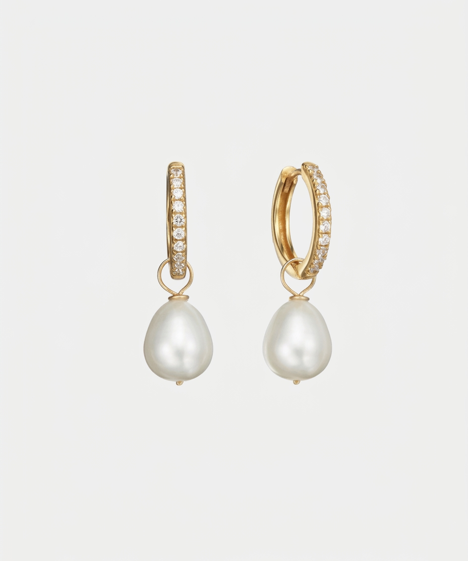 A pair of gold huggie hoop earrings adorned with small pavé-set clear stones and dangling baroque white pearls, shown on a light gray background.